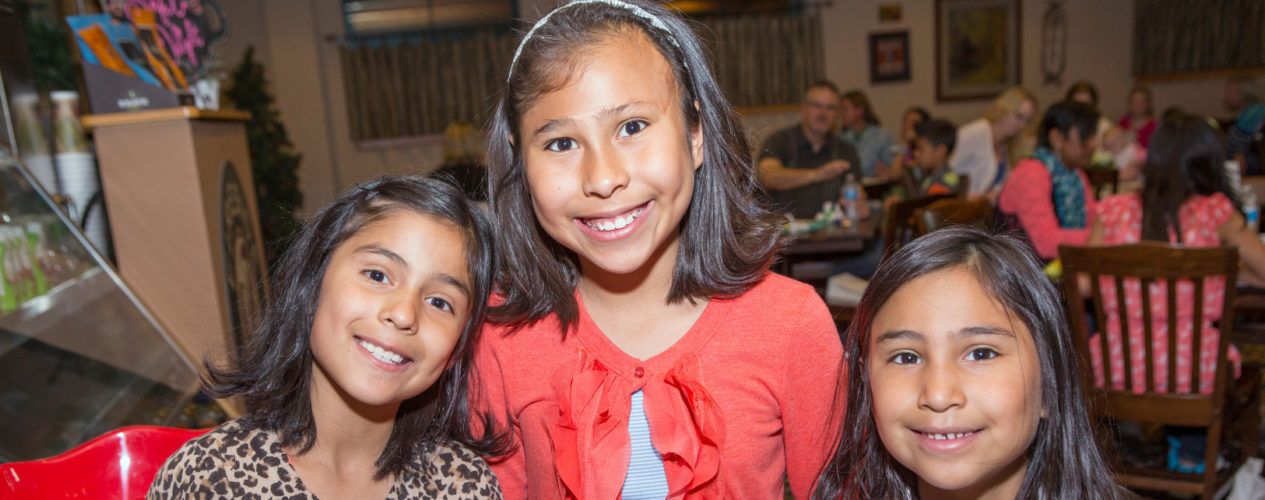 Three girls ranging from early elementary to preteen smile for a photo.