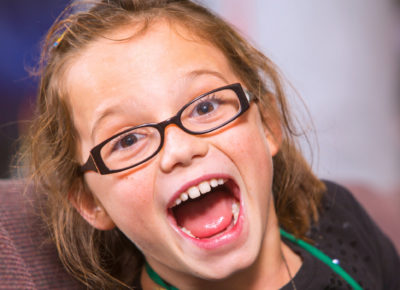 An elementary girls smiles excited, with her mouth wide open, at the camera.
