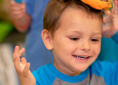 A preschool boy is holding something he made out of non-toxic playdough on top of his head.