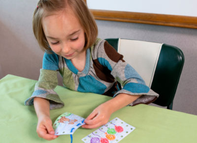 A preschool girl is sitting at a table working on her sewing cards.