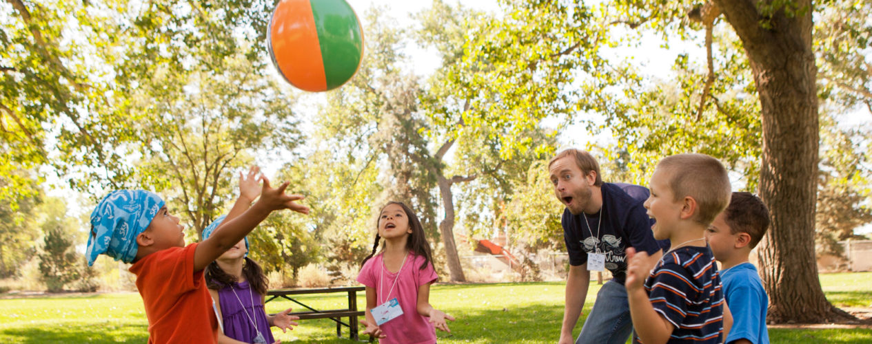 A group of preschoolers are playing an icebreaker outside with an inflatable beach ball.