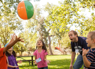 A group of preschoolers are playing an icebreaker outside with an inflatable beach ball.
