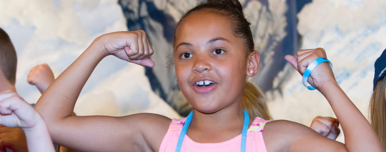 A preteen girl flexes her muscles during a strongman relay game.