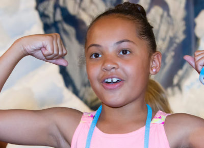 A preteen girl flexes her muscles during a strongman relay game.