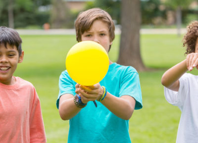Three preteen boys stand in a line. The middle boy is holding a balloon.
