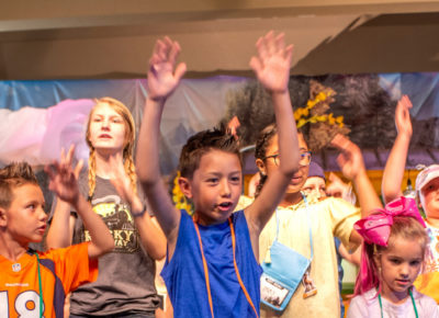 A group of preteens raising their hands in worship as they make a joyful noise to the Lord.