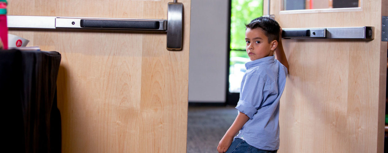 Elementary age boy is walking out a push-open door.