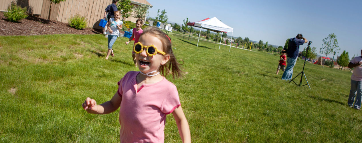 An elementary aged girl wearing sunglasses running around outside at a kite flying event.