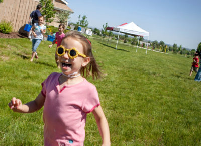 An elementary aged girl wearing sunglasses running around outside at a kite flying event.