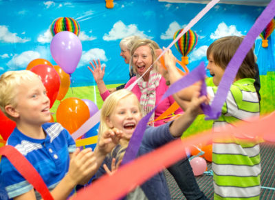 A group of children excitedly celebrate as streamers and balloons fall from the sky.