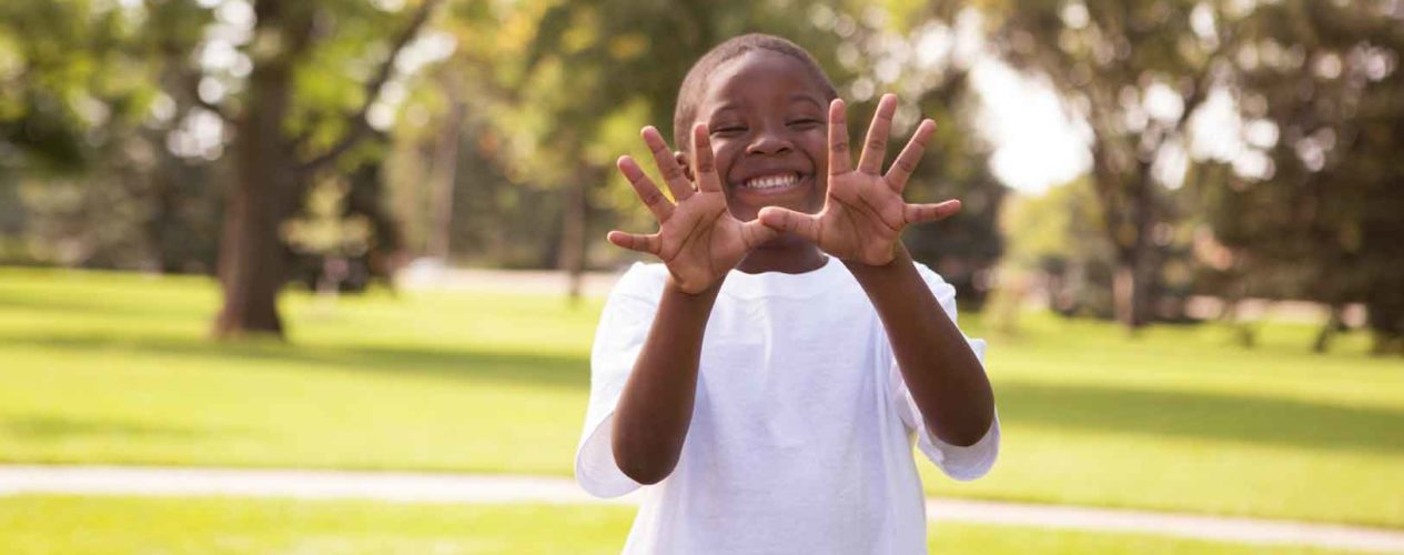 Elementary boy has a huge smile as he gives jazz hands by his face.