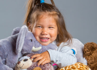 A toddler girl has an arm full of stuffed animals.