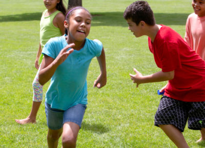 A group of older elementary kids running around outside while playing a game of tag.