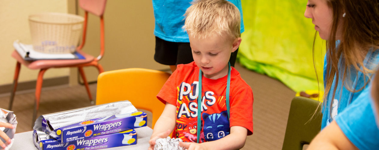 A preschool-aged boy is participating in a craft that involves recycled tin foil.