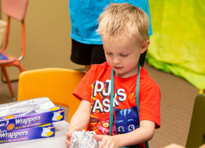 A preschool-aged boy is participating in a craft that involves recycled tin foil.