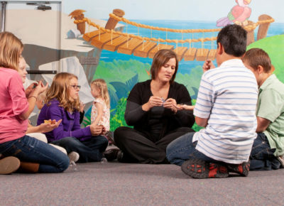 A small group is participating in a milk cap craft as they sit in a circle on the floor.