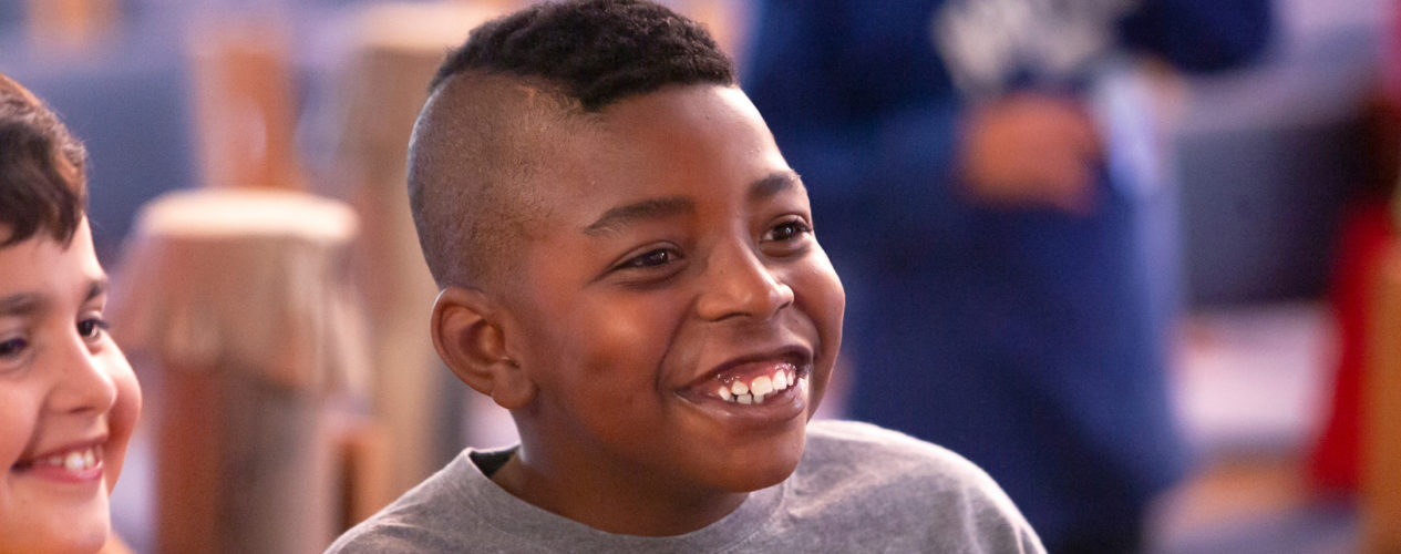 A preteen boy with Tourette Syndrome smiles as he participates in a large group activity.