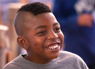 A preteen boy with Tourette Syndrome smiles as he participates in a large group activity.