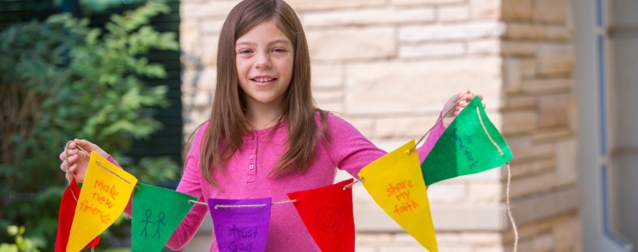 A preteen girl holding colorful pennants outside.