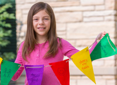 A preteen girl holding colorful pennants outside.
