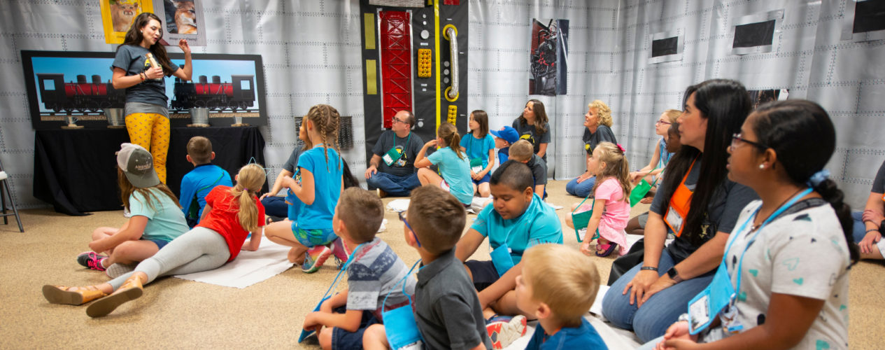 A group of children and volunteers gather in a children's ministry classroom.