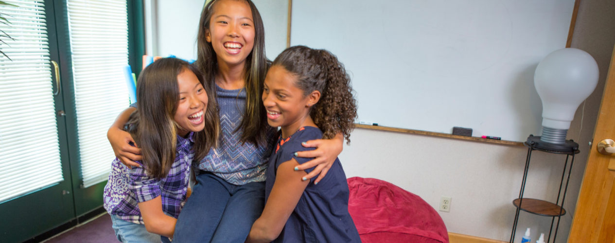 Three preteen girls are playing a Bible game where two girls are lifting the third.