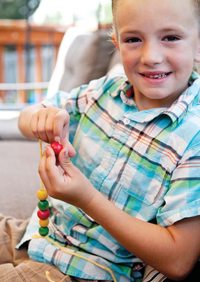 An elementary-aged boy putting beads on a necklace.