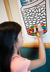 An elementary-aged girl coloring in a picture of vitamins.