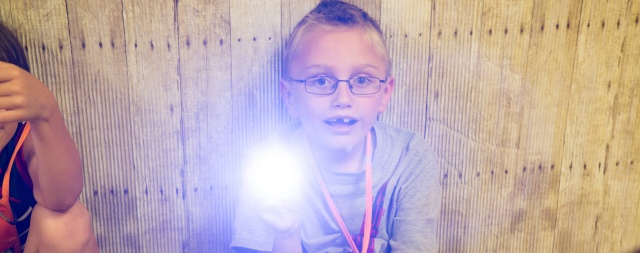 An elementary aged boy holding a flashlight as he participates in a Bible memory activity.