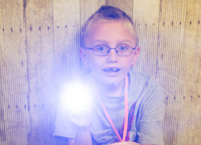 An elementary aged boy holding a flashlight as he participates in a Bible memory activity.