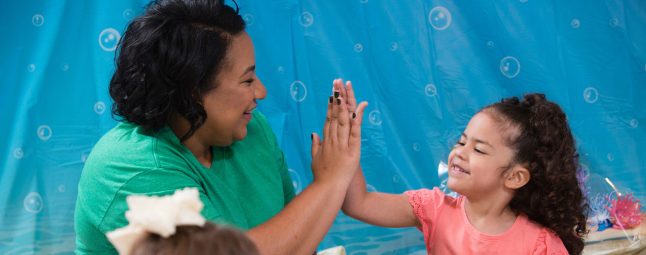 A female volunteer gives an elementary girl a high five during their body image object lesson.