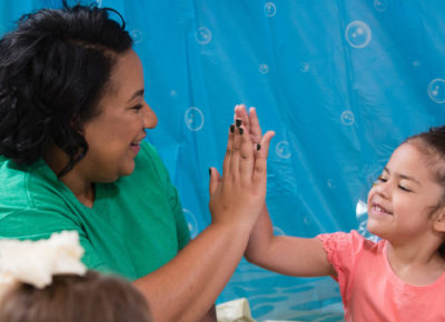 A female volunteer gives an elementary girl a high five during their body image object lesson.