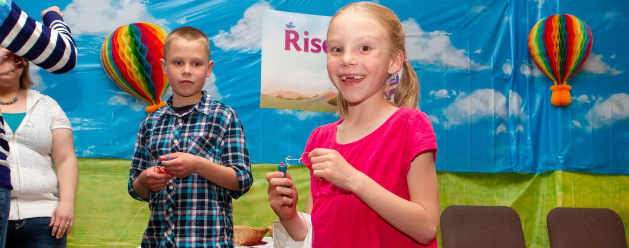 Two children looking excited as they stand in front of an Easter back drop.