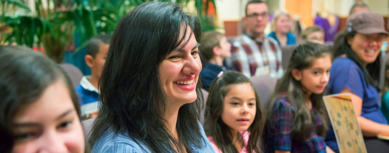 A mom sits smiling next to her daughter as a group of families sit in the sanctuary.