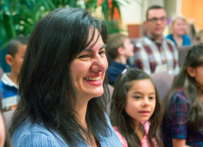 A mom sits smiling next to her daughter as a group of families sit in the sanctuary.