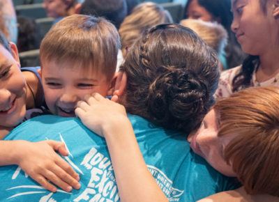 A children's ministry leader hugs her small group of students.