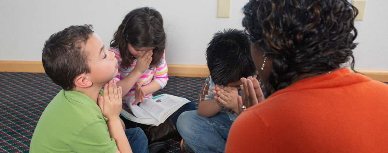 A group of elementary kids praying during a lesson.