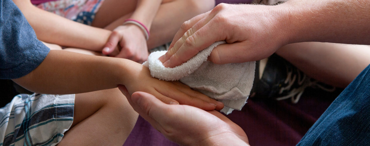 An adult is washing a child's hands with a washcloth.