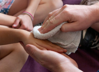 An adult is washing a child's hands with a washcloth.