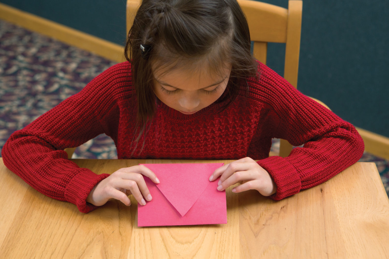 Girl holding a red piece of construction paper that's been folded into an envelope.