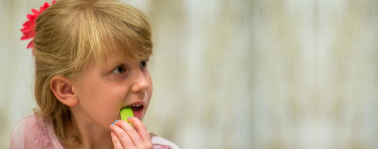 An elementary-aged girl eating a healthy snack of celery.