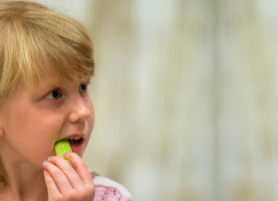An elementary-aged girl eating a healthy snack of celery.