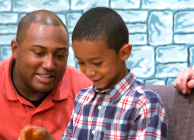 A dad and son are sitting at a table participating in an activity.