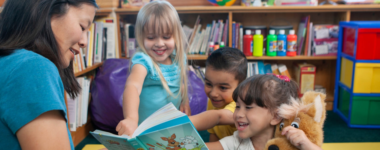 A female teacher reading the Bible two three early elementary kids.