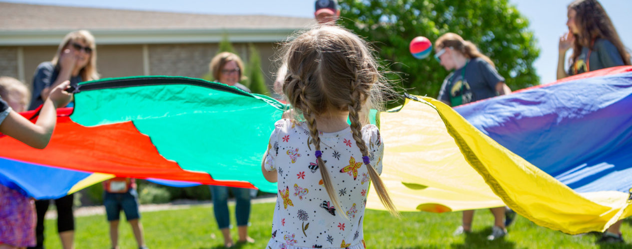 A preschool girl playing outside with a parachute.