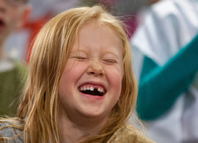 A girl laughing with her eye closed tightly. She is missing a front tooth.