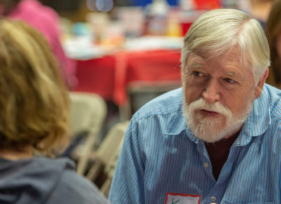 An older male volunteer talking sitting a table with a few other volunteers.