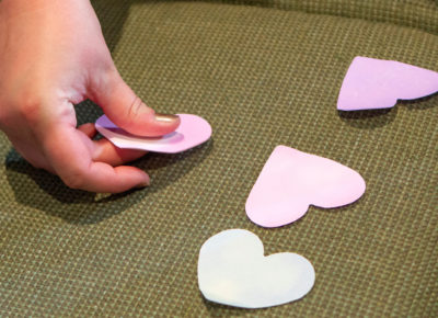 A kid's hand is moving four different prayer hearts around on a chair.