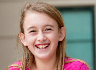 Preteen girl in a pink shirt smiles at the camera.