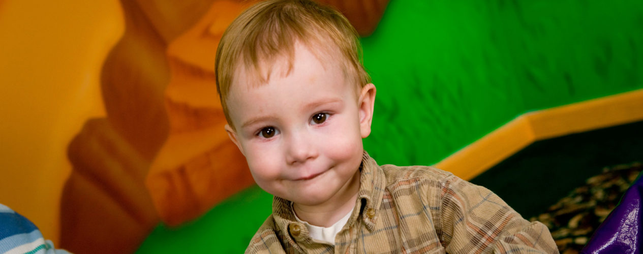 Toddler boy smiling inside a classroom.